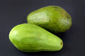 Green avocado on a black background. One peeled avocado and one green. Avocado without peel.