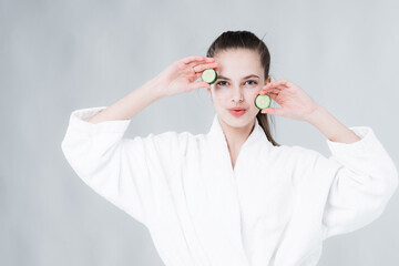 A woman with a clean face makes a cucumber face mask by applying it to her face. Home care