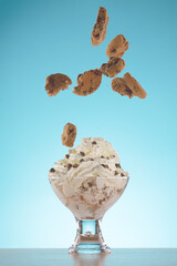 Chocolate chip sundae with falling cookies on it in a studio shot over light blue background