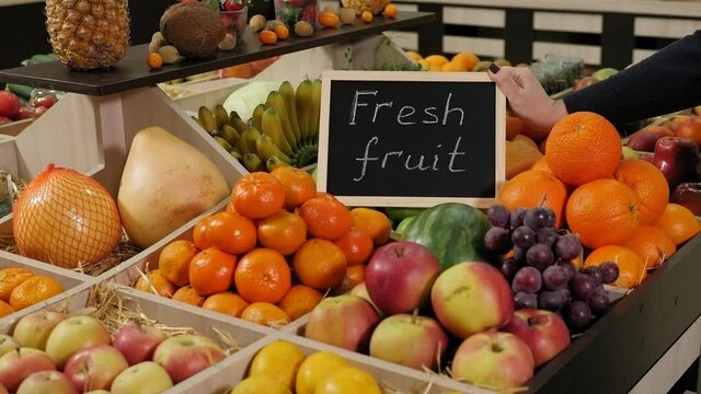 Close-up of a grocery store clerk puts a nameplate with the inscription FRESH FRUIT on a fruit shelf.