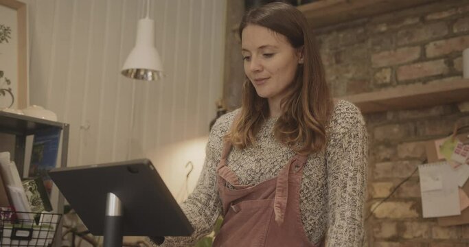 Female retail clerk working cash register in store wearing dungarees