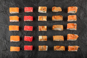 Set of delicious traditional sushi rolls on black surface