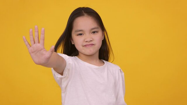 Stop children abuse. Little asian girl gesturing stop, showing palm to camera and shaking head, orange studio background