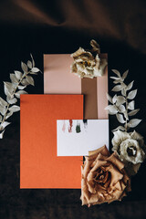 Wedding details. Invitation cards, flowers and rings of the bride and groom lie on a dark textured fabric
