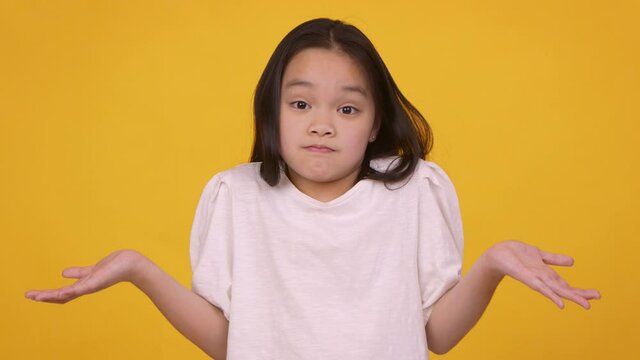 Doubtful asian girl shrugging her shoulders and outstretching hands in ignorance, orange studio background