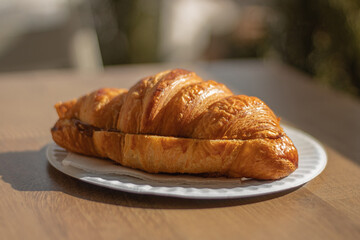 baked croissant with milk jam on a white paper plate with a napkin on a wood table under a sunny light with a blurred background