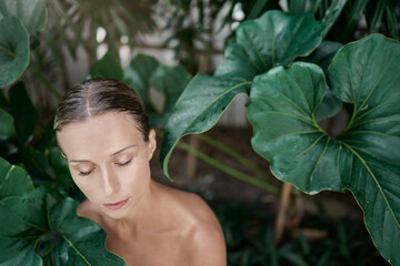 Close up outdoor portrait of young beautiful woman against green tropical leaves.