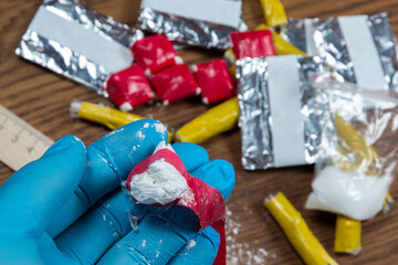 Fototapeta na wymiar evidence of smuggling traffic: Packaging of a narcotic substance in the hand of a forensic expert against the background of other arrested materials, cocaine, heroin, spice