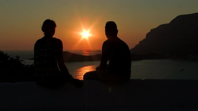 A romantic couple injuring the sunset in Kalymnos in the background the island of Telendos and the face of a princess as the legend says curved on the mountain