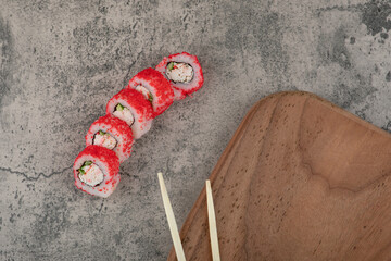 California sushi rolls with a wooden board and chopsticks on stone table