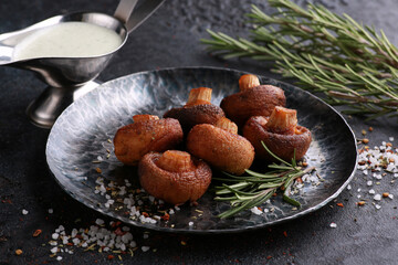 Grilled mushrooms in a black plate with rosemary, spices and white sauce. Restaurant menu, background image, copy space, horizontal