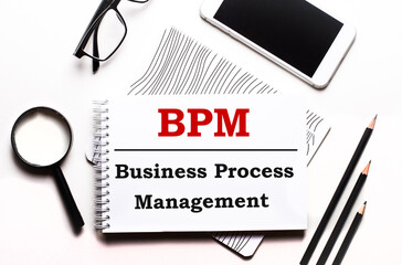 On a white background glasses, a magnifier, pencils, a smartphone and a notebook with the text BPM Business Process Management