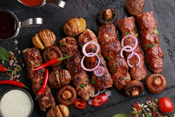 Assorted fried meat and grilled vegetables. Shish kebab, lula, potatoes, mushrooms with  sauce on a black board on table.Fresh tomatoes, chili peppers, onions, herbs and spices. Background, top view