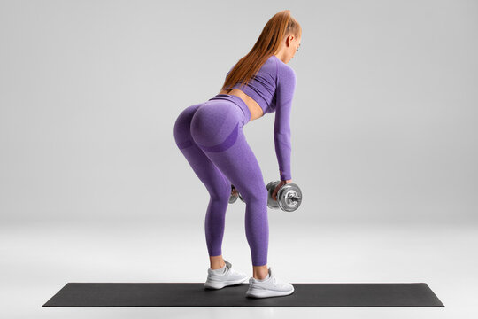 Fitness woman doing deadlift exercise for glutes on gray background. Athletic girl working out with dumbbells