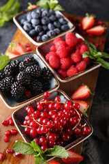 Fresh berries. Red currants, blackberries, blueberries and raspberries in bowls on a large wooden board with mint leaves, strawberries and pomegranate seeds. Background image, top view, closeup