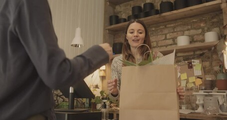 Retail clerk giving paper shopping bag with purchase to customer in store