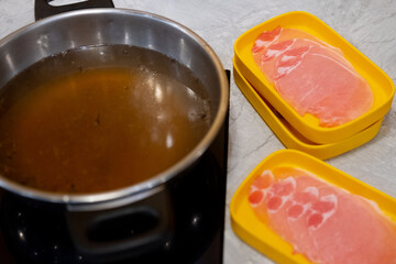 Thinly sliced of raw pork on yellow tray with hot soup in pot prepare for customer cook.