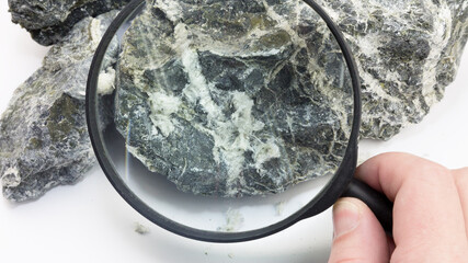 Hand with magnifying glass examines asbestos fibers in stone.,