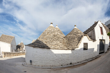 Fototapeta na wymiar Typical street in Alberobello, a Trulei village, with white houses with a tapered stone roof. Photo taken with a fisheye lens.