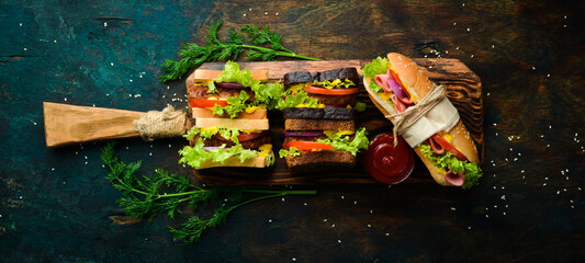 Set of sandwiches and burgers on a wooden kitchen board. On a stone background. Top view.