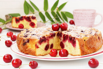 Homemade cut pie with cherries is located on a plate on a white background with cup of coffee.
