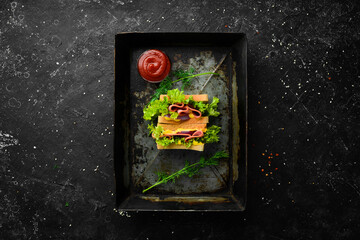 Toast bread sandwich with sausage, onion, cheese and lettuce on a black stone background. Street food. Free copy space.