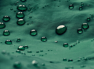 Water drops on waterproof membrane fabric. Detail view of texture of green waterproof cloth.