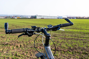 Fototapeta na wymiar A bicycle handlebar seen from the first person perspective. Visible bicycle frame and bicycle accessories on the handlebar and the field in the background..