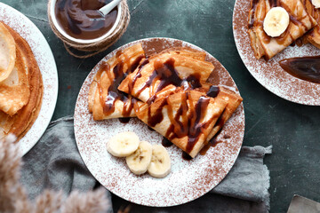 Sweet breakfast. Thin pancakes with caramel, chocolate and banana. Dark background. Top view.