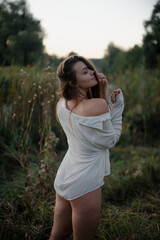 Fototapeta premium Sexy girl in a white shirt on nature in the evening in the sunset rays of the sun