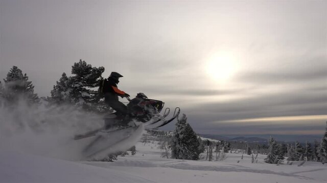 SLOW MO: video footage of jumping snowmobilers at sunset. the snowmobile flies through the air and creates large and beautiful swirls of snow. ProRes 422. HD 500fps
