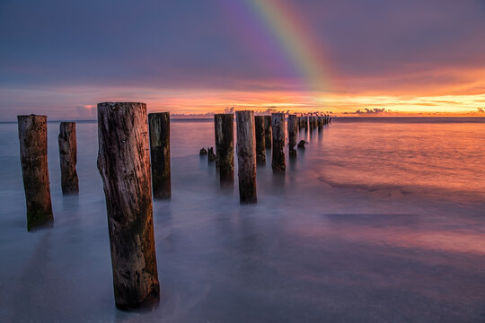 Old wooden jetty, pier, during sunset on the sea. Dramatic sky with rainbow. Beauty of nature concept.