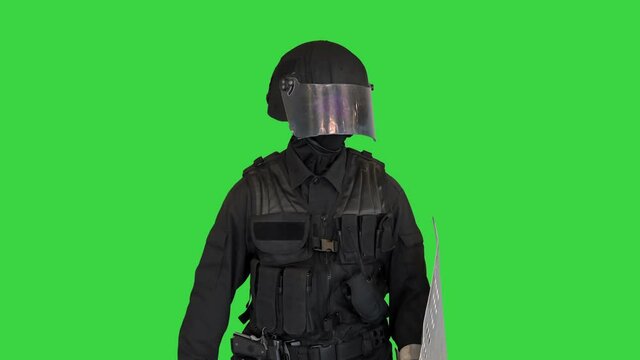 Riot police man with tactical baton and a shield standing and touching his face on a Green Screen, Chroma Key.