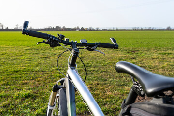 Fototapeta na wymiar A bicycle handlebar seen from the first person perspective. Visible bicycle frame and bicycle accessories on the handlebar and the field in the background.