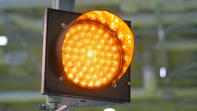 Close up view: single signal LED orange traffic light blinking at transport exhibition, trade show. Danger, warning, safety, attention concept