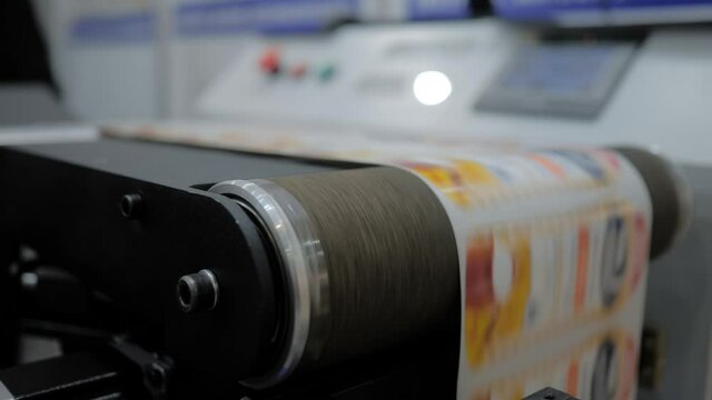 Conveyor of slitter rewinding inspection machine with fast moving printed labels at printer exhibition, trade show - close up. Technology, manufacturing, food packaging, advertising concept