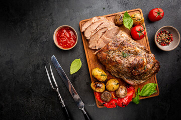 Baked pork meat with grilled vegetables on a cutting board on dark background, top view