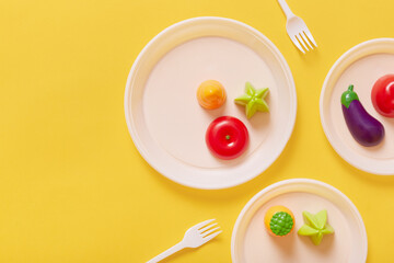 Top view of eggplant, tomatoes, carrots on white plates, two forks, artificial plastic food,...