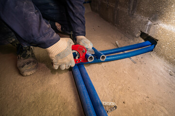 a hand cuts through a plastic heating pipe, with special scissors in gloves on the concrete floor