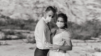 Fototapeta premium Young loving couple in medical masks in park during quarantine on wedding day.