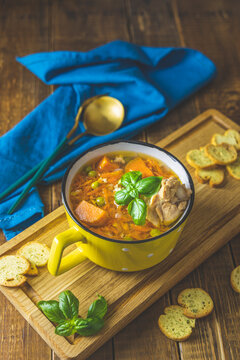 Homemade chicken vegetable soup with carrots and sweet potatoes, on wooden board over rustic wooden table background. Shallow depth of field.