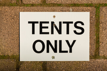 Close up of a white tents only sign on a brick wall at a campsite