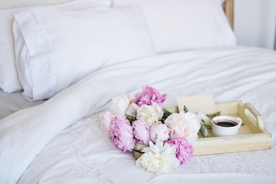 Close-up of a tray with a Bouquet of peonies, cup of coffee and an envelope on a bed