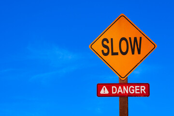 Sign "Slow Danger" to show the way to dangerous car pass keeping walking, save yourself and another people on blue sky background.