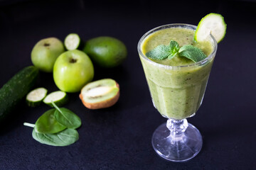 Delicious green smoothie and fresh fruits on black table. Healthy green smoothie with banana, spinach, avocado, apple and mint in a glass. Vegan food.