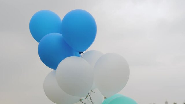Colorful helium balloons swaying in wind against gray overcast sky at summer city festival - slow motion, close up view. Street decoration, celebration, art, holiday concept