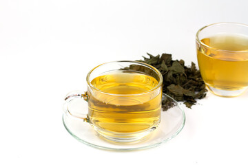 Tulsi or holy basil tea in transparent cup with pile of dried tulsi leaf isolated on white background. Ayurvedic medicine in India. Drink for health.