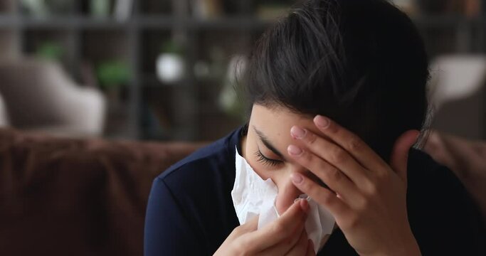 Head shot unhealthy unhappy millennial mixed race indian woman using paper tissue, suffering from runny nose sinusitis nasal infectious disease, feeling uncomfortable at home, first grippe symptoms.