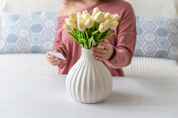 Woman pulling blank greeting card from bouquet of white tulips flowers. Mother day