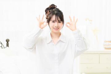部屋でOKのジェスチャーをする白いシャツを着た若い女性